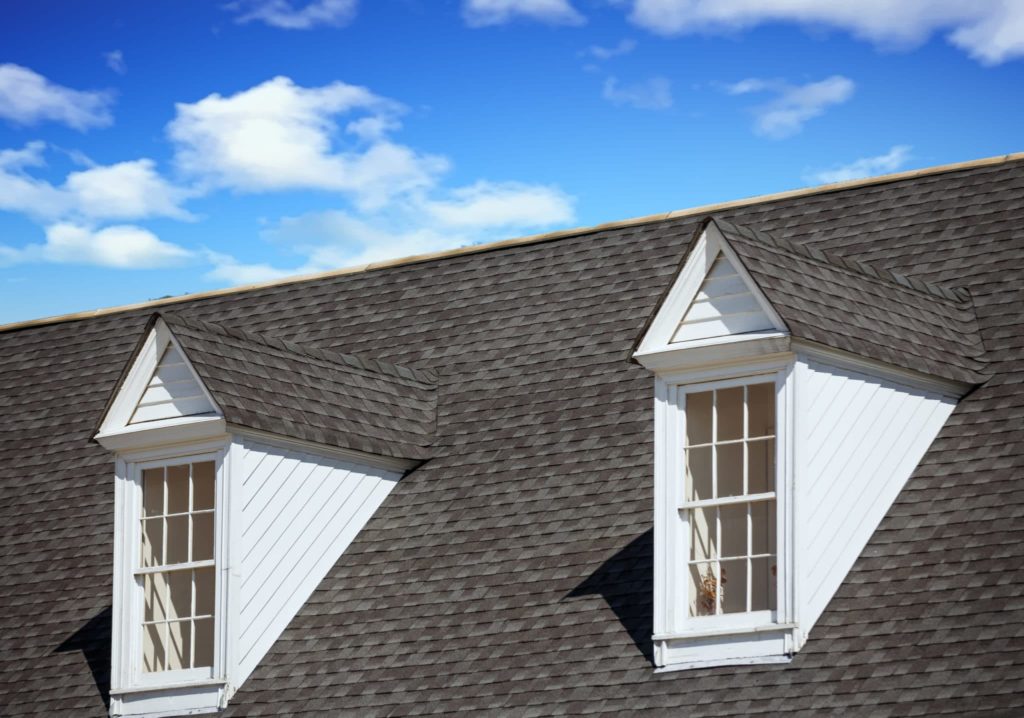 Two white wood dormers on a grey shingle roof under blue sky