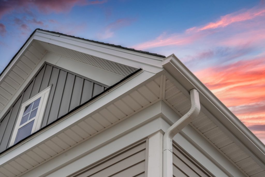 A blue home with new roofing and gutters against a sunset sky.