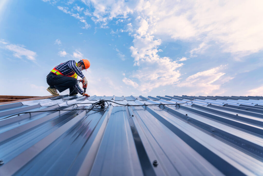 Roof construction concept, Roofer using air or pneumatic nail gun and installing on new roof metal sheet.