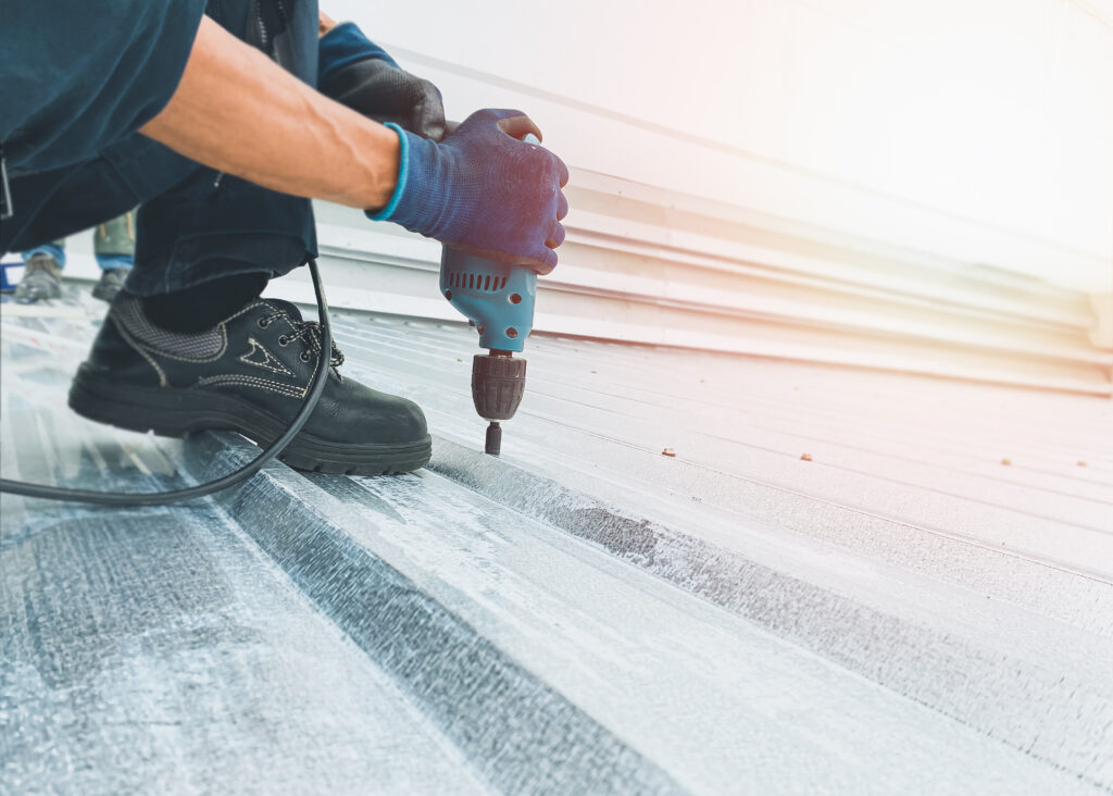 Workers wearing protective gear are screwing nuts on the metal roof with electric drills to install or repair with professional expertise, an orange light shines through