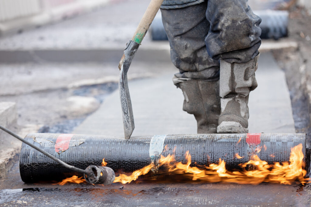 Waterproofing Works. Construction worker applying SBS Modified Bitumen Roll Sheet over a Concrete Bridge Deck with Butane Gas Blow Torch