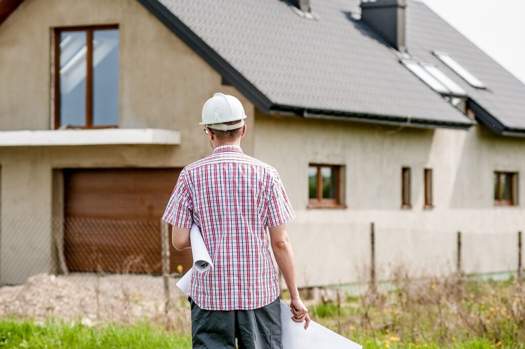 An individual wearing a hard hat stands in front of a house, holding a blueprint. The image implies construction and planning, with a mention of a tax deduction for a new roof.