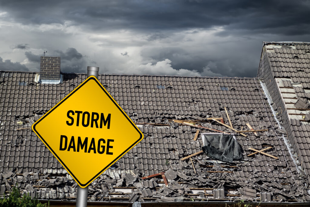 yellow storm damage prevention warning sign in front of roof of house damaged by heavy hurricane tornado storm.