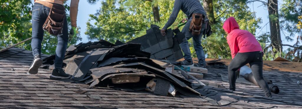 A group of workers removing old shingles from a roof during a roofing repair project.
